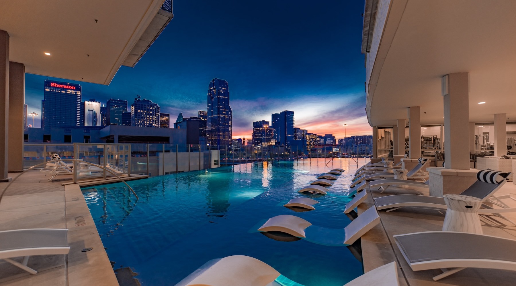 Relax and unwind poolside a pool with chairs around it and a city in the background