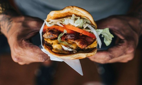 man holds a thick, juicy burger with both hands