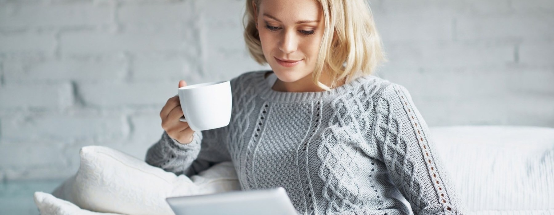 a woman looking at an device and holding a cup
